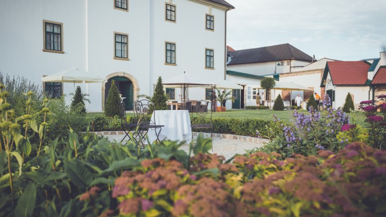 Garden view of Raggendorf Castle with flowers, tables and chairs in the foreground.