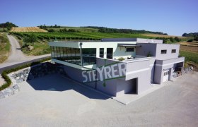 Modern Steyrer winery with glass fa&ccedil;ade and surrounding vineyards.