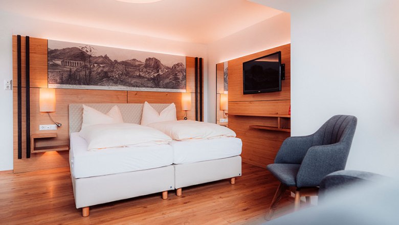 Modern hotel room with double bed, wooden floor and wall decoration.