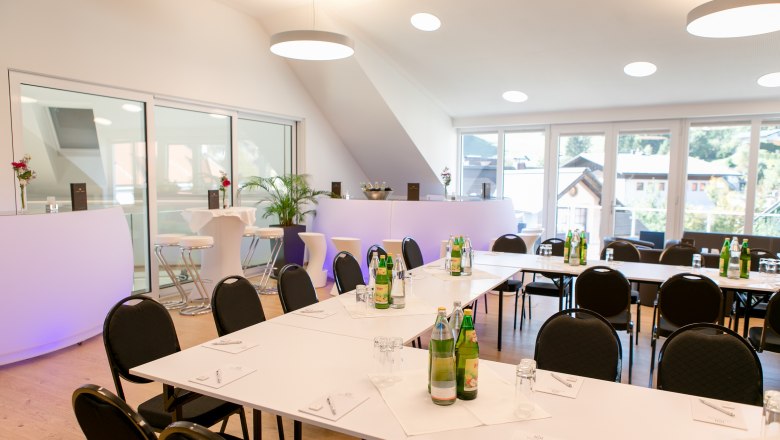 Modern seminar room with white tables, chairs and drinks, large windows with a view outside.