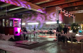 Interior view of an event room with an old streetcar, tables and lighting.