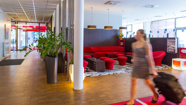 Hotel lobby with red sofa and woman with suitcase.