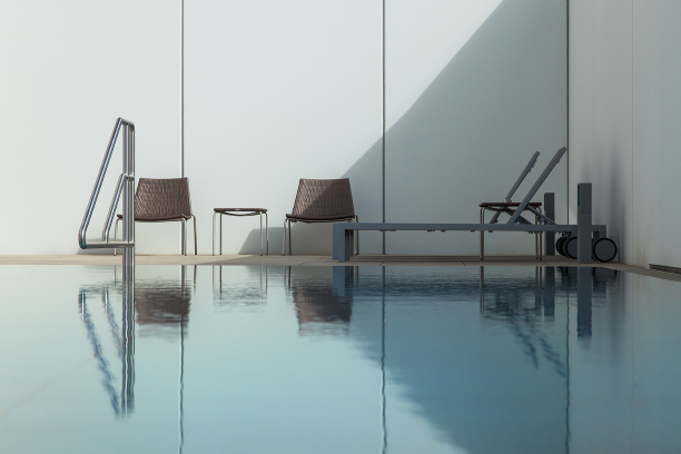 Modern outdoor pool with two chairs and a lounger against a white wall.