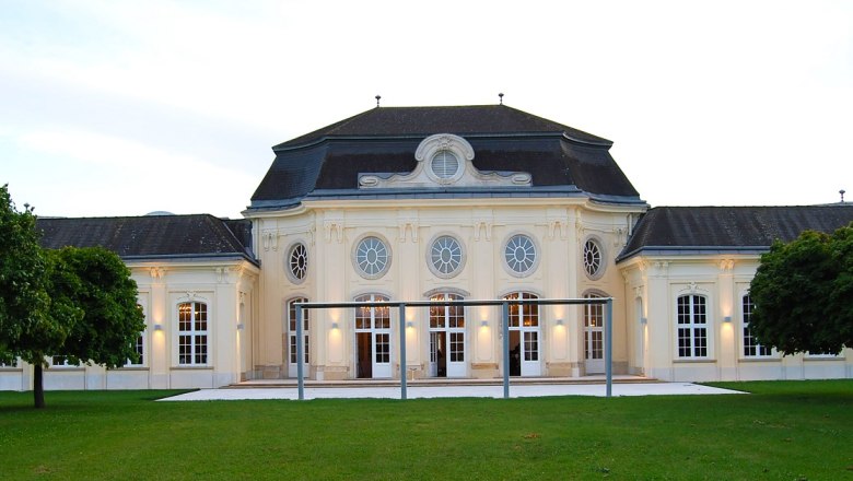 Historic building with symmetrical façade and large windows, surrounded by green spaces.