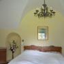 Bedroom with double bed, yellow walls, a chandelier and flowers in a vase.