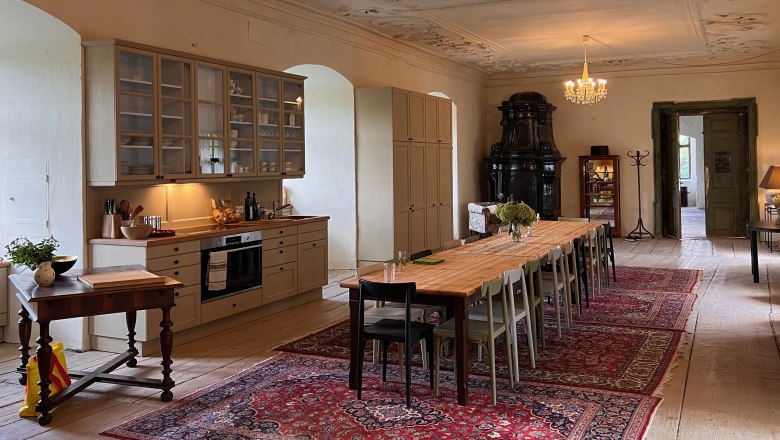 Elegant dining room with long wooden table, chandeliers and antique stove.