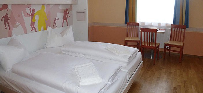Hotel room with double bed, two chairs and a table in front of a window.