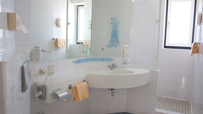 Bright bathroom with washbasin, mirror, shower and towels.