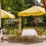 View of a terrace with yellow parasols and a laid table, surrounded by green countryside.