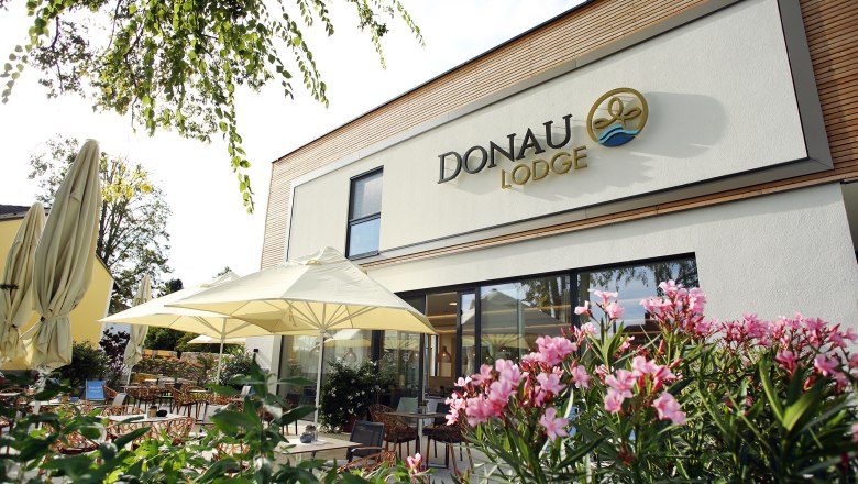 Exterior view of the Donaulodge with terrace, parasols and flowering plants.