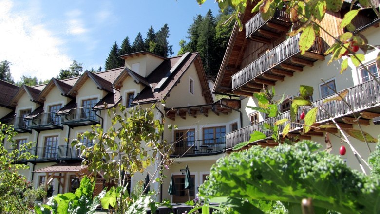 An alpine-style building with balconies, surrounded by lush greenery and plants.