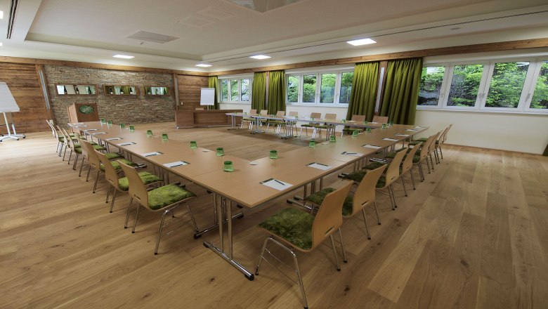 Seminar room with U-shaped table arrangement, green chairs and large windows.