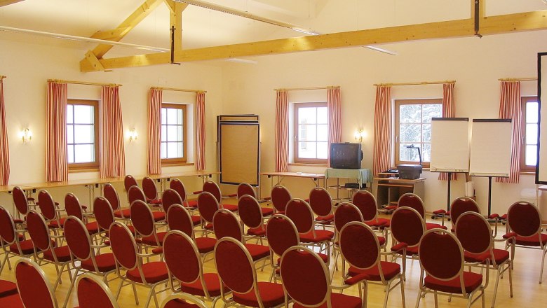 A conference room with red chairs, wooden beams and windows with striped curtains.