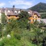 A large building with a wooden fa&ccedil;ade, surrounded by lush greenery and a mountain in the background.