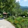 A well-kept garden with a gravel path, flower beds, a pavilion and sun loungers against a mountain backdrop.