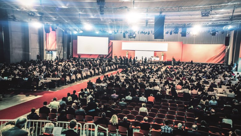 Large congress hall with many participants, stage and screen.