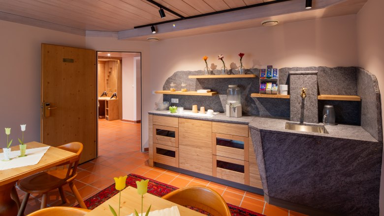 A cozy lounge in a hotel spa with wooden furniture, a small kitchenette and decorative flowers.
