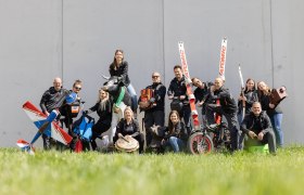Group of people posing with sports equipment and a cow statue on a meadow.