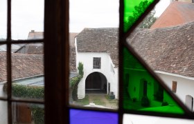 View through a stained glass window of an old courtyard with an arched gate and tiled roofs.
