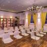 A conference room with white chairs, yellow curtains and a chandelier.