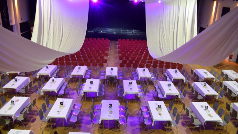 An event room with tables and chairs, purple lighting and a stage in the background.
