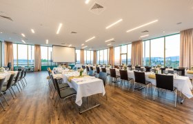 A large, bright room with covered tables and chairs, large windows and a projector.