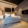 Modern bedroom with wooden floor, gray wall, double bed and flat screen TV.