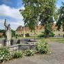 View of a historic castle complex with statue and garden.