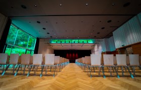 Interior view of a modern event room with empty rows of chairs and a stage in the background.