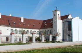 Katzelsdorf Castle with modern extension and historic building. White façade with rounded windows, red roof and large inner courtyard