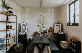 A stylishly furnished room with a wooden table, shelves, plants and works of art on the walls.