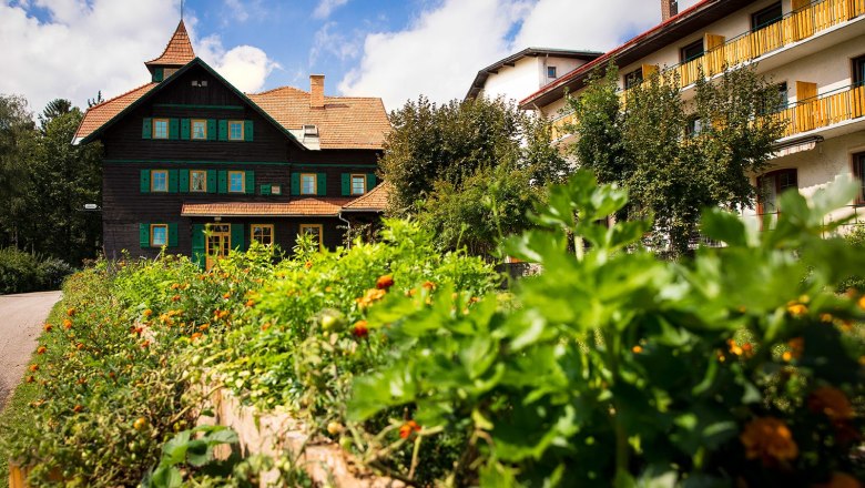 A traditional building with green shutters and a garden in the foreground under a blue sky.