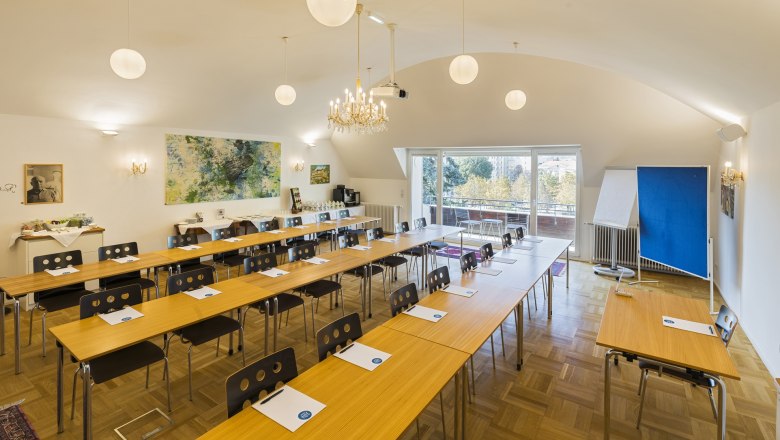 A conference room with tables and chairs, a chandelier and a large window with a view outside.