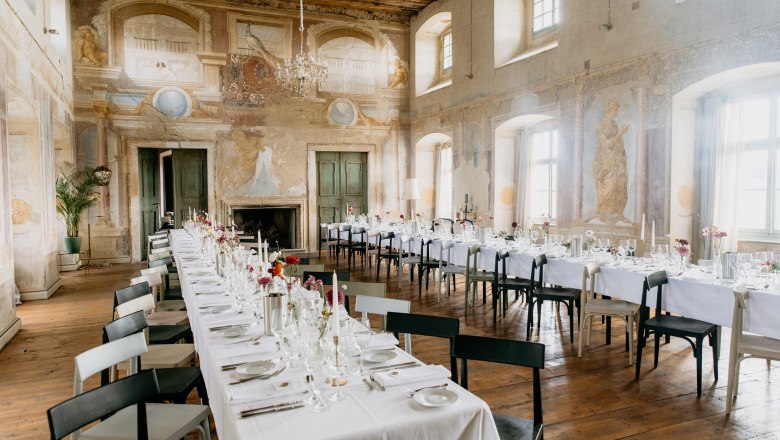 Elegant dining room in a castle with long, laid tables and murals.