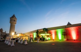 Outdoor evening event with illuminated building and tents.