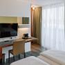 Modern hotel room with desk, TV and curtains.