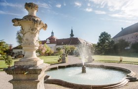 Fountain in the garden of Seitenstetten Abbey with baroque architecture in the background.