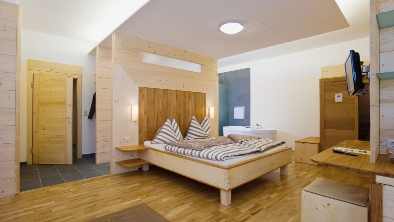 Wooden interior of a modern hotel room with double bed and bathtub.