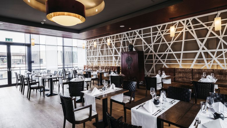 Elegant restaurant with modern Asian design elements, laid tables and large windows.