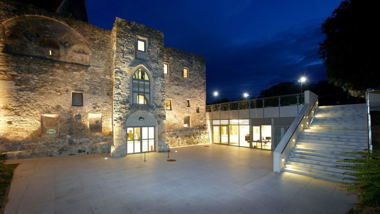 Illuminated Perchtoldsdorf Castle at night with modern extension and staircase.