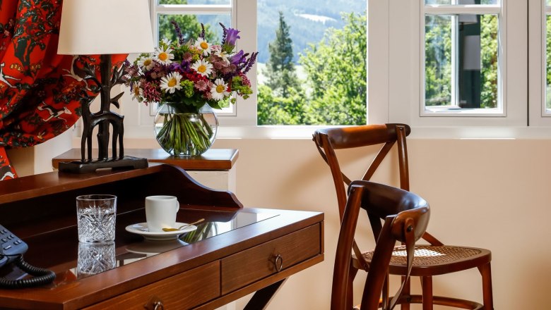 An elegant room with wooden furniture, a desk, chairs and a window overlooking a green landscape.