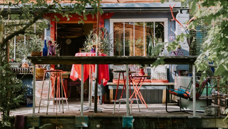 Colorful terrace in front of the location with red chairs and table, surrounded by plants and decorations.