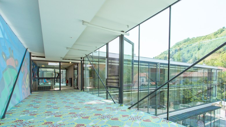 Modern, glazed passageway with colorful carpet and wall art.