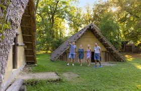Four people stand outside a historic building with a thatched roof.