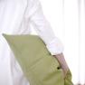 Person in white shirt holding a green cushion in front of a bright window.