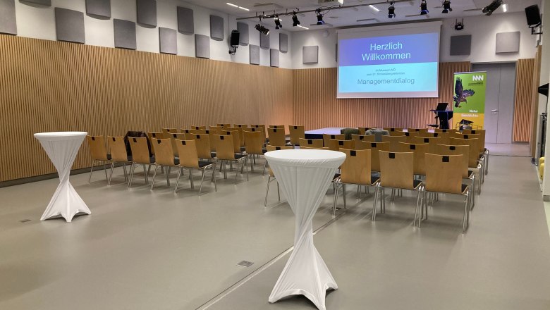 Conference room with rows of chairs, bar tables and a screen with the inscription 'Welcome'.