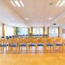 A bright seminar room with rows of chairs, large windows, and a projector mounted on the ceiling.