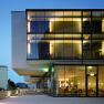 Modern hotel building with glass fa&ccedil;ade at dusk, illuminated interiors visible.