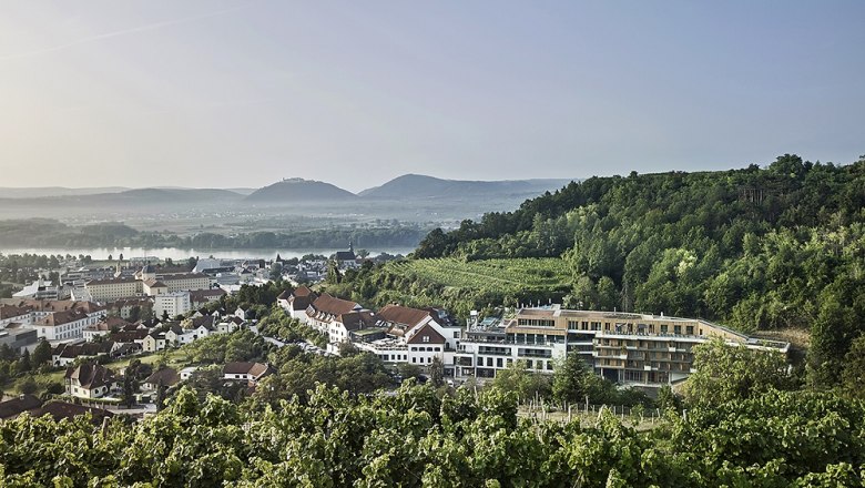 View of the Steigenberger Hotel & Spa Krems surrounded by vineyards and hills.