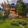 An illuminated building with a garden and sun loungers at dusk.